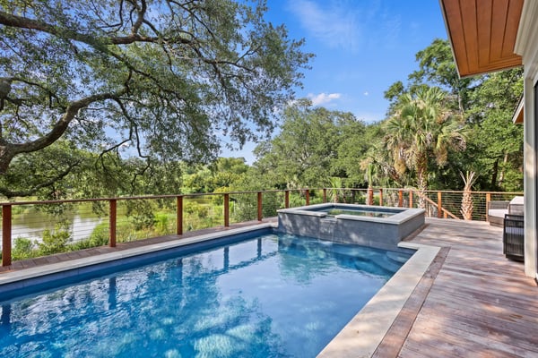 Waterfront deck with swimming pool, hot tub, and river view surrounded by mature trees and palm trees