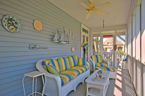 Rooftop deck with black Adirondack chairs, metal railing, and sunset view over coastal neighborhood with ocean in distance