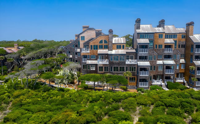 Beachfront vacation rental homes with cedar shingle siding and metal roofs nestled among coastal vegetation and dunes.